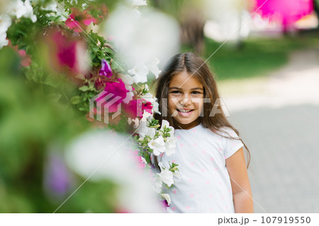 Cheerful little girl smiles among the flowers in summer Cheerful little girl smiles among the flowers in summer 107919550