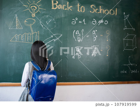 Education. Back view of school girl on science lesson in classroom write an answer on blackboard, primary child is standing in front of class in school writing chalkboard, Back to school concept Education. Back view of school girl on science lesson in classroom write an answer on blackboard, primary child is standing in front of class in school writing chalkboard, Back to school concept 107919599