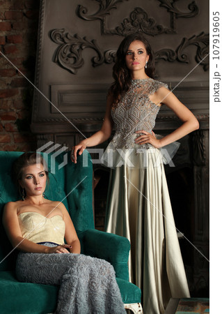 Vogue style models. Gorgeous women wearing evening gown posing in hotel room Vogue style models. Gorgeous women wearing evening gown posing in hotel room 107919605