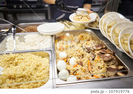A traditional Uzbek dish called pilaf. Rice with meat, carrots, onions, quail eggs and kazy . Glass Showcase in a buffet or self-service restaurant. 107919776