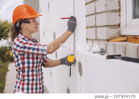Insulation of the house with polyfoam. The worker is checking with the construction level the accuracy of the installation of polystyrene board on the facade. 107924570