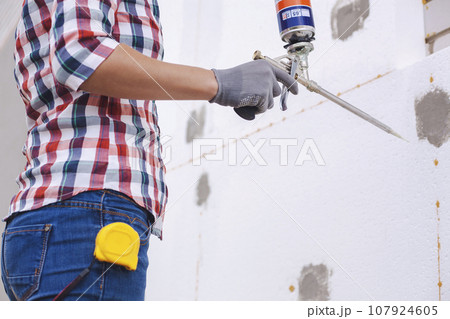 Insulation of the house with polyfoam. worker foaming joints of polystyrene board on the facade. Insulation of the house with polyfoam. worker foaming joints of polystyrene board on the facade. 107924605