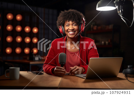 African American woman recording a blog in the studio, wearing headphones in front of a microphone, recording podcasts, blogging 107924931