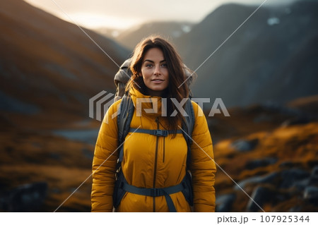 A beautiful girl in a yellow jacket with a backpack walks in the mountains. A girl in a yellow jacket travels in the mountains. travel concept A beautiful girl in a yellow jacket with a backpack walks in the mountains. A girl in a yellow jacket travels in the mountains. travel concept 107925344