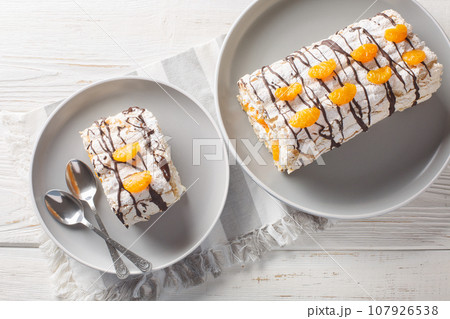 Delicious homemade Swedish dessert Budapest roll cake filled with whipped cream and mandarins close-up in a plate on the table. Horizontal top view Delicious homemade Swedish dessert Budapest roll cake filled with whipped cream and mandarins close-up in a plate on the table. Horizontal top view 107926538