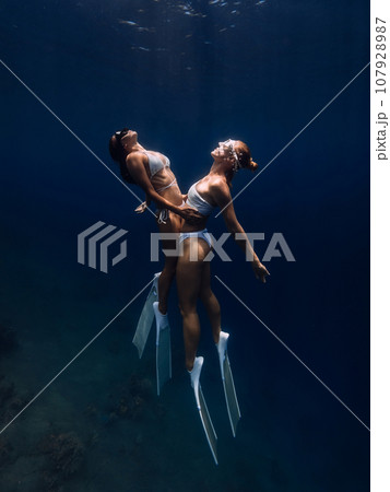 Girlfriends freedivers hugging and dives in deep ocean. Freediving with couple ladies in underwater 107928987