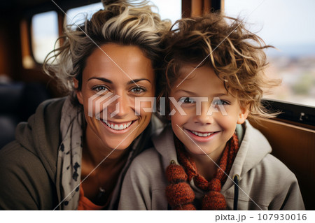 Close-up portrait of a beautiful woman and her son in a train carriage. Cheerful, smiling mother and boy are going on a trip, enjoying the time spent. Recreation, travel and entertainment. 107930016