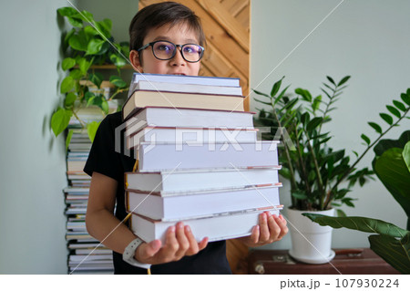 A boy holds a stack of books against the background home library. 107930224