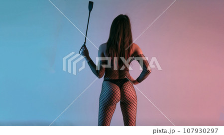 Sexy lady in bdsm outfit. Beauty woman standing back with spank ridding crop 107930297