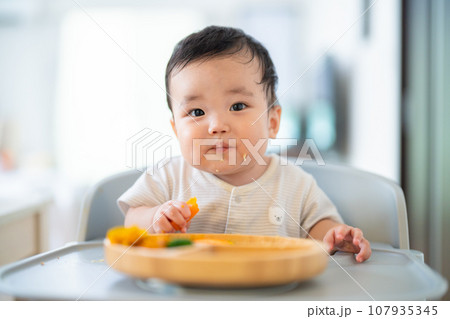 離乳食後期でをつかみ食べをしてご機嫌な生後9か月の赤ちゃん 離乳食後期でをつかみ食べをしてご機嫌な生後9か月の赤ちゃん 107935345