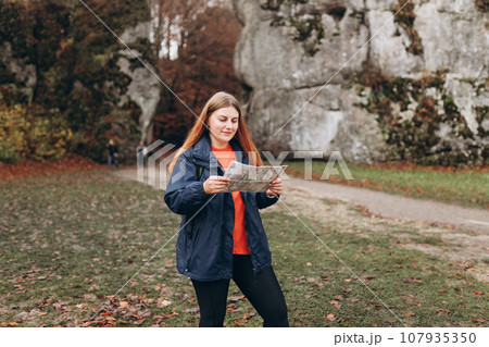 Portrait of positive cheerful girl holding paper map over nature background. Mountain peaks. Freedom, happiness, travel and vacations concept, outdoor activities 107935350