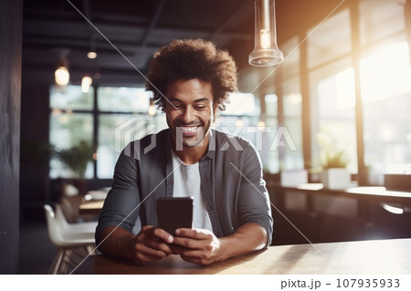 Portrait of cheerful African American businessman in casual clothes with smartphone at a table. Happy smiling mature man, successful entrepreneur or employee working in office or coworking cafe. 107935933