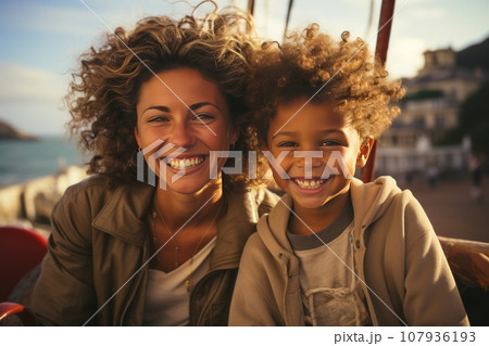 Close-up portrait of a beautiful woman and her son riding an amusement park ride. Cheerful, smiling mother and boy relaxing and enjoying time. Shared leisure and entertainment strengthens family ties. 107936193