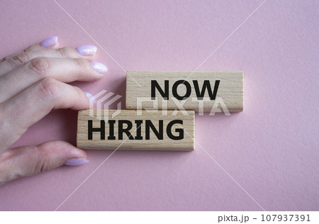 Now Hiring symbol. Concept word Now Hiring on wooden blocks. Businessman hand. Beautiful pink background. Business and Now Hiring concept. Copy space 107937391