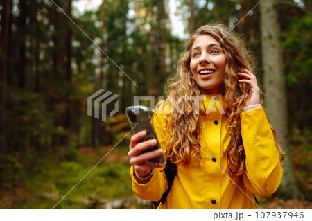 Travel apps. Curly young woman traveler in yellow coat holding smartphone in hand. Concept of travel 107937946