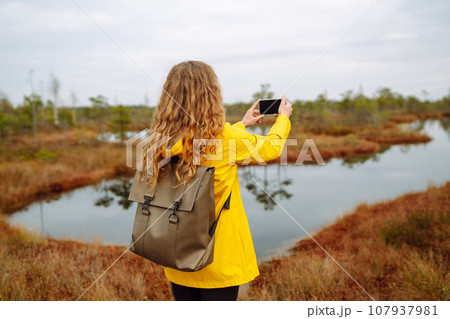 Tourist travels in nature, photographs landscapes in swamps using mobile phone. Active lifestyle. Tourist travels in nature, photographs landscapes in swamps using mobile phone. Active lifestyle. 107937981