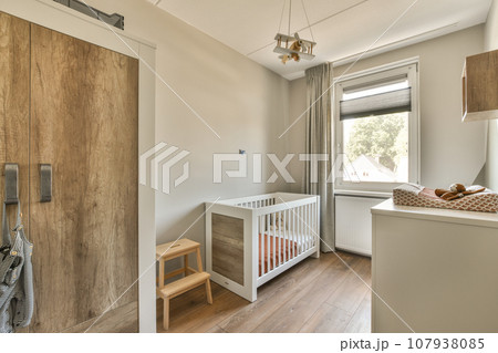 a baby's room with a cribt in the corner and an open door leading to another room 107938085