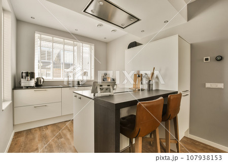 a kitchen and dining area in a modern apartment with wood flooring, white cupboards and wooden bar stools 107938153