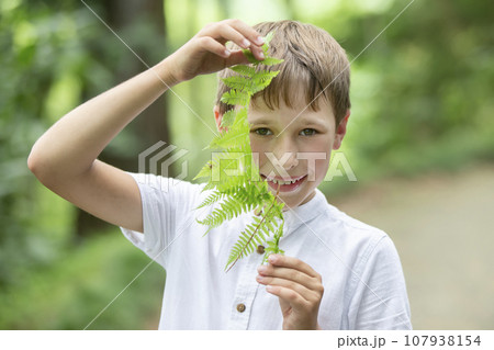 A handsome young boy shows a fern leaf. Child with a plant. 107938154