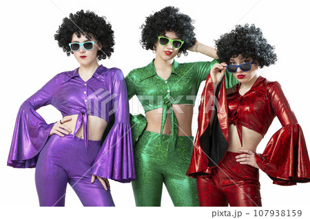 A group of disco girls in African American wigs and colorful costumes on a white background. Fashion of the seventies and eighties. 107938159