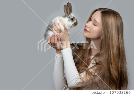 Happy young girl holding a white rabbit on a gray background 107938160