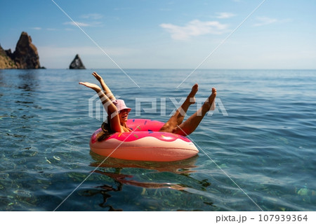 Summer vacation woman in hat floats on an inflatable donut mattress. Happy woman relaxing and enjoying family summer travel holidays travel on the sea. 107939364