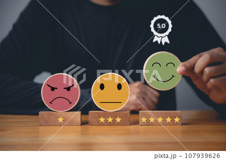 Hand choosing a smiley face on a wooden block circle to rate the best business services and customer experience. Satisfaction survey and 5-star rating concept. Hand choosing a smiley face on a wooden block circle to rate the best business services and customer experience. Satisfaction survey and 5-star rating concept. 107939626