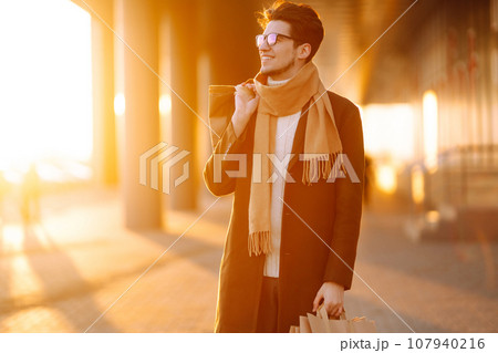 Stylish man with paper packages after shopping at sunset. Handsome man doing shopping. Stylish man with paper packages after shopping at sunset. Handsome man doing shopping. 107940216