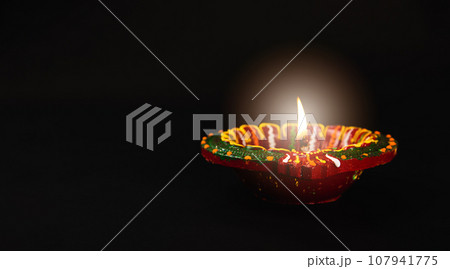 In the spirit of Diwali, vibrant clay diya lamps, symbols of prosperity and happiness, cast their glow on a tranquil black background. Perfect for invitations, text overlays, and abstract art. 107941775