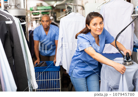 Female laundry worker ironing clean clothes in cleaning salon 107945780