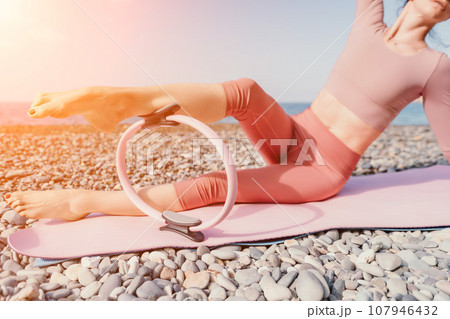 Woman sea pilates. Sporty happy middle aged woman practicing fitness on beach near sea, smiling active female training with ring on yoga mat outside, enjoying healthy lifestyle, harmony and meditation Woman sea pilates. Sporty happy middle aged woman practicing fitness on beach near sea, smiling active female training with ring on yoga mat outside, enjoying healthy lifestyle, harmony and meditation 107946432