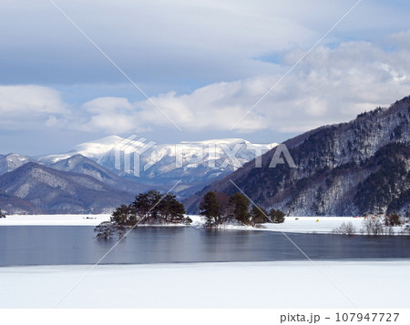 雪解けの始まった福島県、秋元湖。白い雪原と青い湖面、遠方に冠雪の箕輪山が印象的で綺麗だ。 107947727