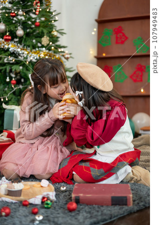 Two cute and joyful young Asian girls are enjoying eating sweets and celebrating Christmas together. 107949483