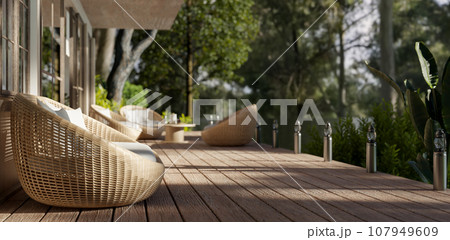 Side view of a beautiful deck with cosy round wicker armchairs and a beautiful green nature view. 107949609