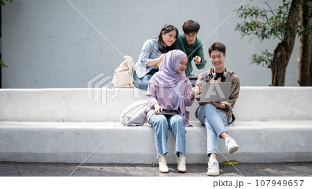 A group of happy, diverse Asian students working on a project while sitting outdoors together. 107949657