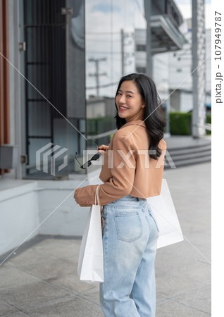 An attractive Asian woman is walking outside of a shopping mall with her shopping bags. An attractive Asian woman is walking outside of a shopping mall with her shopping bags. 107949787
