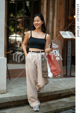 A trendy Asian woman is walking down the stairs with her shopping bags, enjoying her shopping day. 107949814