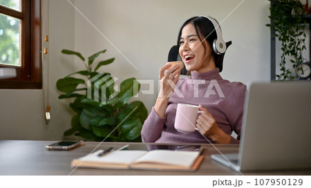 Beautiful Asian girl eating a donut while studying at her study table in her house 107950129