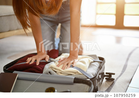 Close-up image of a woman packing her overfilled suitcase for her summer holiday trip. Close-up image of a woman packing her overfilled suitcase for her summer holiday trip. 107950259