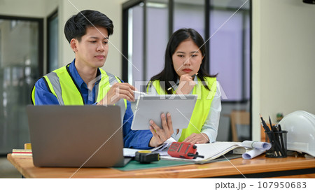 Two professional and serious Asian engineers are looking at a tablet screen, discussing work 107950683