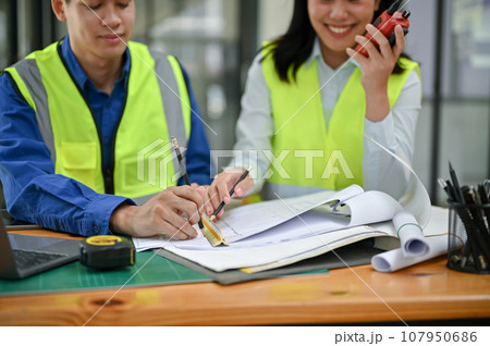 Two professional Asian construction engineers are checking a blueprint, discussing work Two professional Asian construction engineers are checking a blueprint, discussing work 107950686