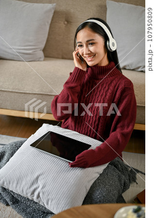 A woman enjoys listening to music while relaxing in her living room on a winter day. 107950809