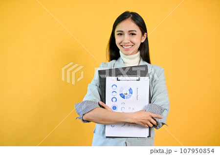 A pretty Asian businesswoman standing against an isolated yellow background with documents A pretty Asian businesswoman standing against an isolated yellow background with documents 107950854