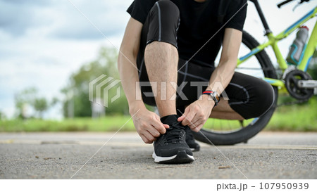 Cropped image of a healthy, fit male cyclist tying his shoelaces before riding a bike 107950939