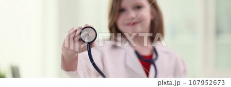 Adorable girl in white lab coat holds stethoscope in hand 107952673