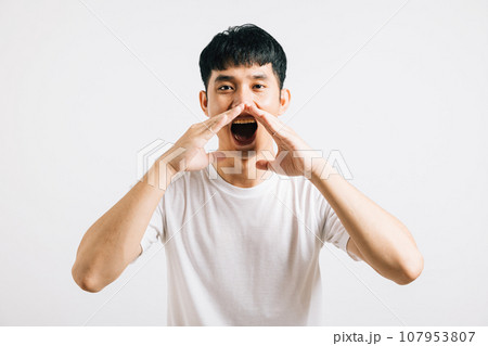 Portrait of a happy Asian young man with his hand on his mouth, sharing exciting news or announcements. Studio shot isolated on a white background, leaving room for copy space. Portrait of a happy Asian young man with his hand on his mouth, sharing exciting news or announcements. Studio shot isolated on a white background, leaving room for copy space. 107953807