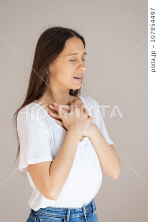 Portrait of confident beautiful woman with long brown hair, wearing casual clothes, standing in relaxed pose with hands on chest, breathing deeply, doing breathing exercise. Portrait of confident beautiful woman with long brown hair, wearing casual clothes, standing in relaxed pose with hands on chest, breathing deeply, doing breathing exercise. 107954497