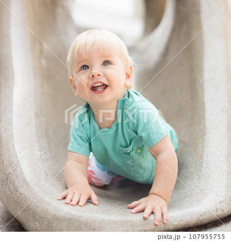 Child playing on outdoor playground. Toddler plays on school or kindergarten yard. Active kid on stone sculpured slide. Healthy summer activity for children. Little boy climbing outdoors 107955755
