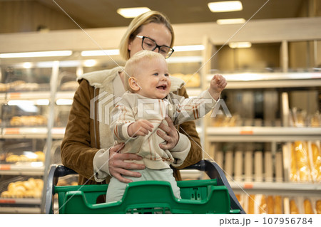 Caucasian mother shopping with her infant baby boy child choosing products in department of supermarket grocery store Caucasian mother shopping with her infant baby boy child choosing products in department of supermarket grocery store 107956784