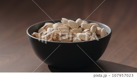 Roasted salted pistachios in black bowl on walnut table 107957023